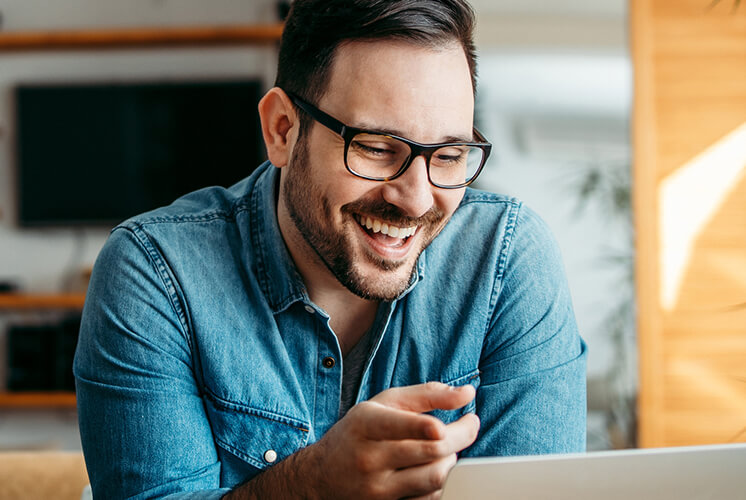 man in denim shirt laughing and using a laptop
