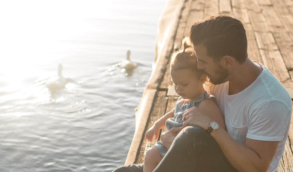 father and daughter sitting on a dock watching ducks