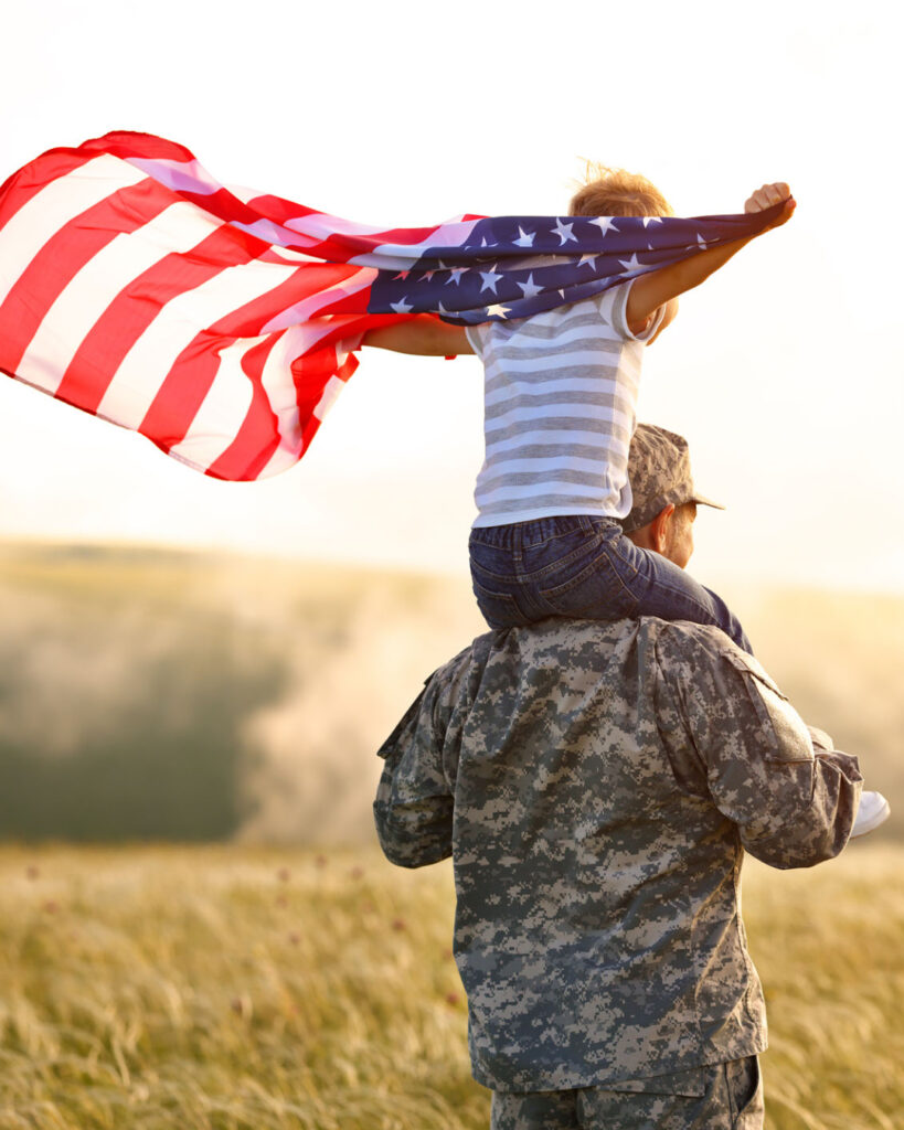 A solider carries a child on his shoulders while the child holds an American flag